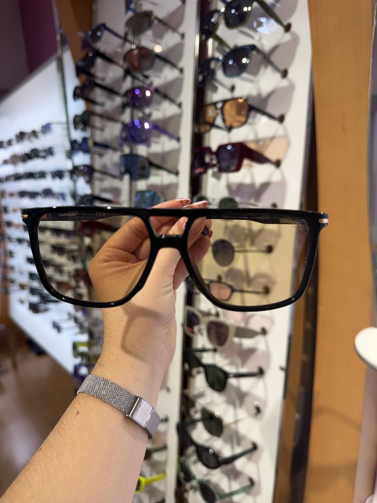 Mano sosteniendo unas gafas delante del expositor