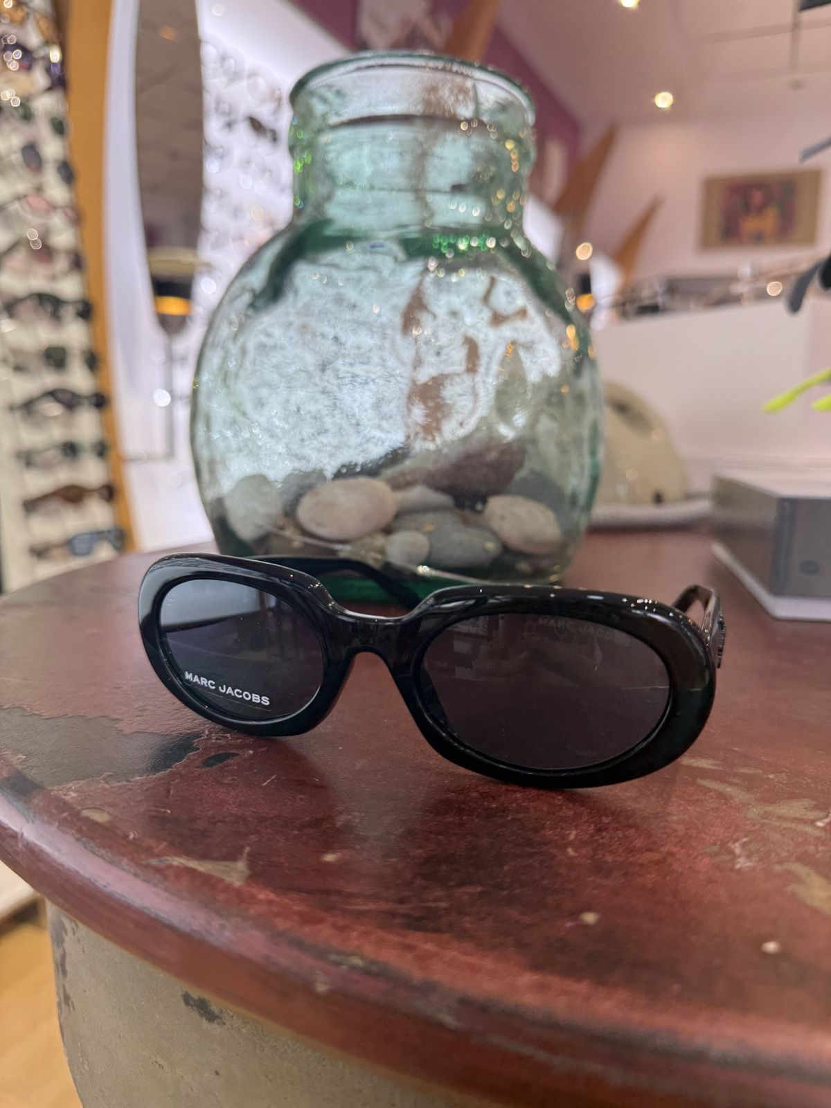Gafas de sol negras junto a un jarrón de cristal verde